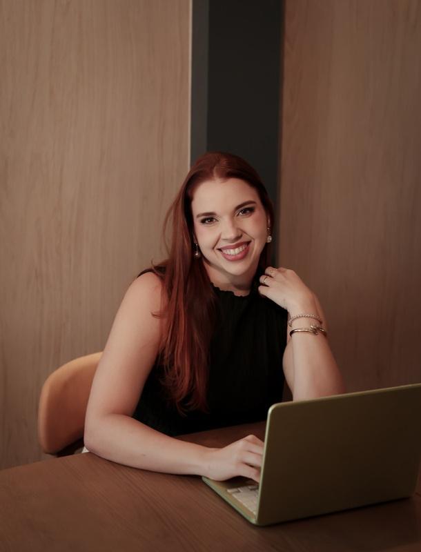 Dra. Bruna Alonso sorrindo, sentada à mesa diante do notebook